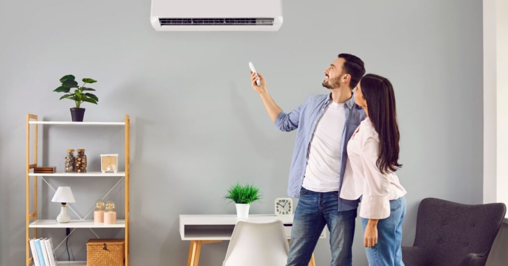 Un couple dans leur salon allume une climatisation murale grâce à une télécommande. 